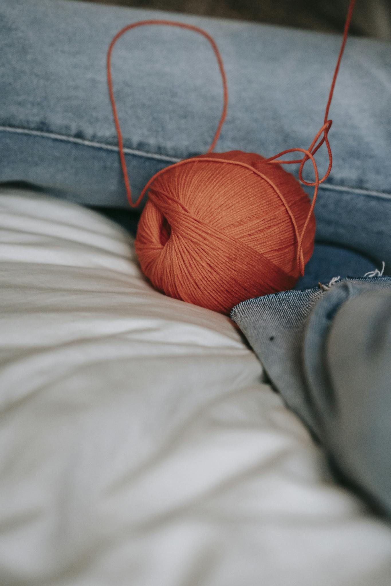 Close-up of an orange yarn ball resting on white linen and denim fabric, perfect for craft and textile themes.