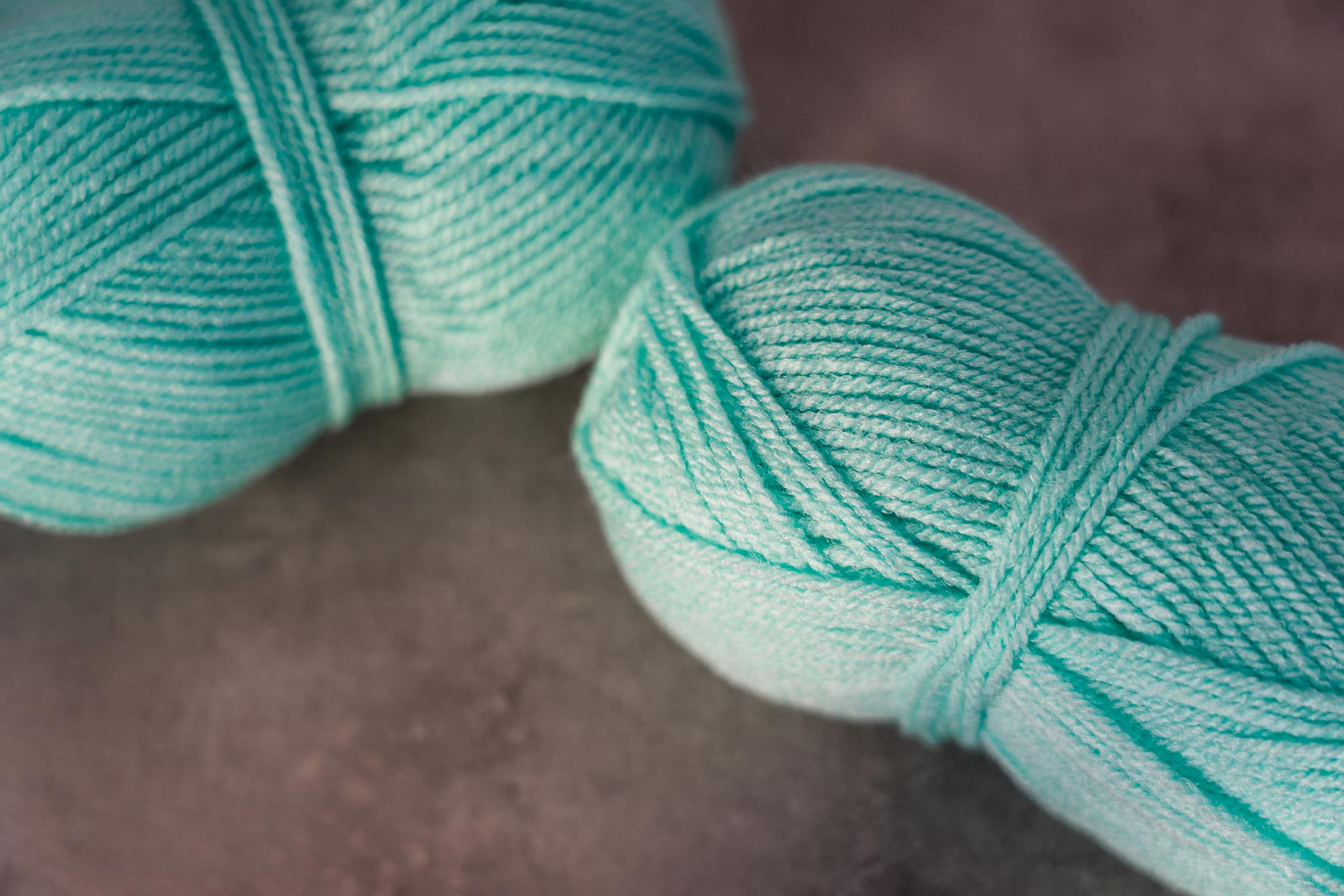 Close-up of two turquoise yarn balls on a textured surface, perfect for crafts.